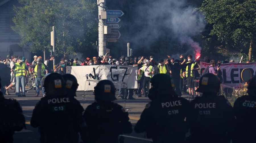 Polisi anti huru hara berjaga-jaga sementara para demonstran memegang spanduk dan suar selama protes menentang KTT G7 yang akan datang di Evian-les-Bains di Prancis, di Jenewa, Swiss, 14 Juni 2026.