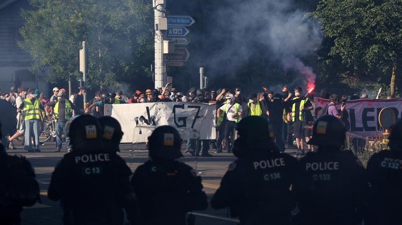 Polisi anti huru hara berjaga-jaga sementara para demonstran memegang spanduk dan suar selama protes menentang KTT G7 yang akan datang di Evian-les-Bains di Prancis, di Jenewa, Swiss, 14 Juni 2026.