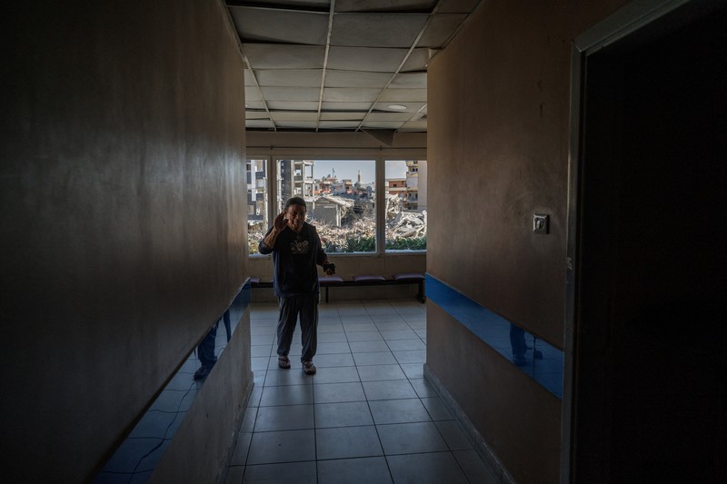 Youssef Fares, 90, whose home of more than 70 years was damaged in an Israeli airstrike, stands at the window of a hospital room where he has taken shelter, overlooking buildings damaged by Israeli strikes, following a deal between the United States and Iran, in Tyre, southern Lebanon, June 16, 2026. REUTERS/Zohra Bensemra.