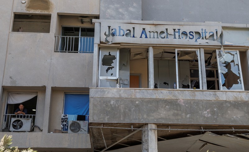 Youssef Fares, 90, whose home of more than 70 years was damaged in an Israeli airstrike, stands at the window of a hospital room where he has taken shelter, overlooking buildings damaged by Israeli strikes, following a deal between the United States and Iran, in Tyre, southern Lebanon, June 16, 2026. REUTERS/Zohra Bensemra.