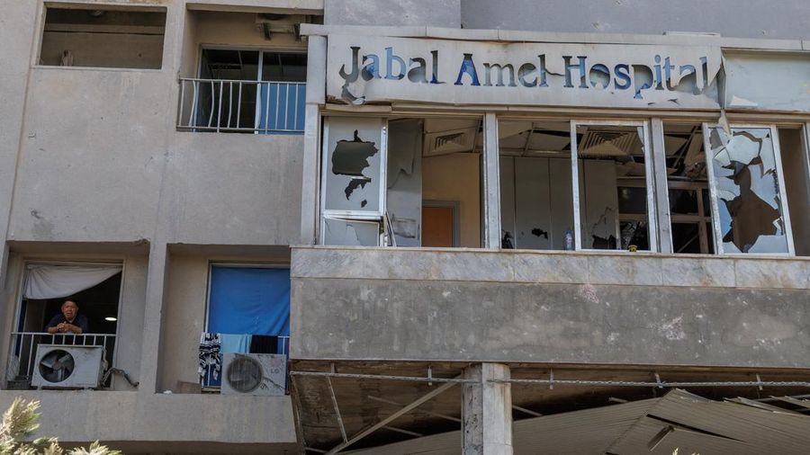 Youssef Fares, 90, whose home of more than 70 years was damaged in an Israeli airstrike, stands at the window of a hospital room where he has taken shelter, overlooking buildings damaged by Israeli strikes, following a deal between the United States