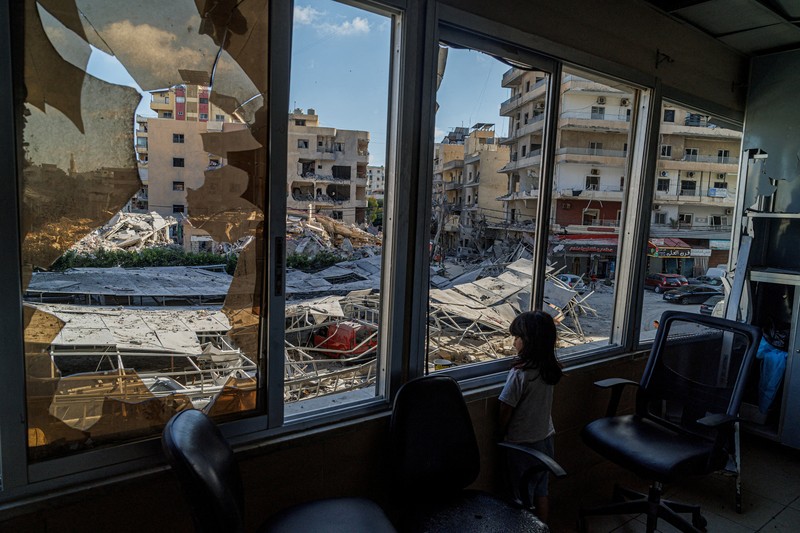 Youssef Fares, 90, whose home of more than 70 years was damaged in an Israeli airstrike, stands at the window of a hospital room where he has taken shelter, overlooking buildings damaged by Israeli strikes, following a deal between the United States and Iran, in Tyre, southern Lebanon, June 16, 2026. REUTERS/Zohra Bensemra.