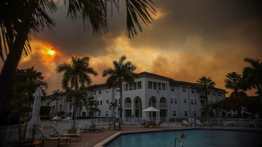 Sebuah keluarga berada di kolam renang komunitas perumahan saat kebakaran semak berkobar relatif dekat dengan lingkungan perumahan Doral di Miami, Florida, AS, 16 Juni 2026.