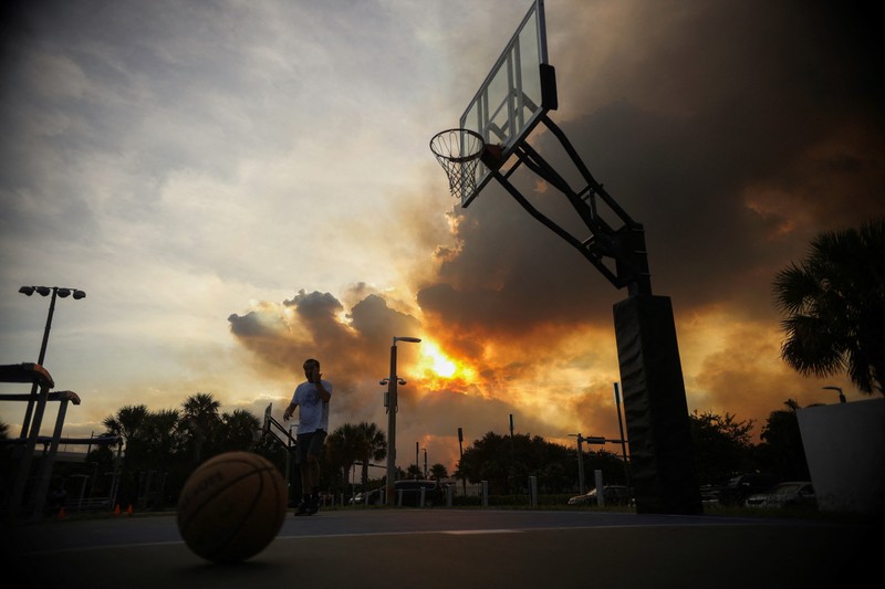 Seorang wanita menutupi wajahnya saat menyaksikan kebakaran semak yang terjadi relatif dekat dengan lingkungan perumahan Doral di Miami, Florida, AS, 16 Juni 2026. (REUTERS/Maria Alejandra Cardona)