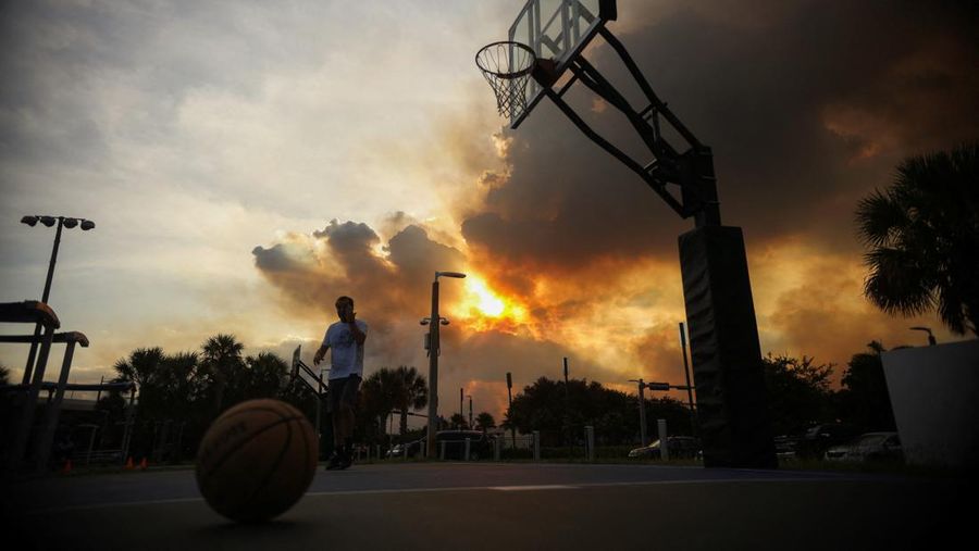 Seorang pria bermain bola basket di Doral Legacy Park saat kebakaran semak berkobar relatif dekat dengan lingkungan perumahan Doral di Miami, Florida, AS, 16 Juni 2026.