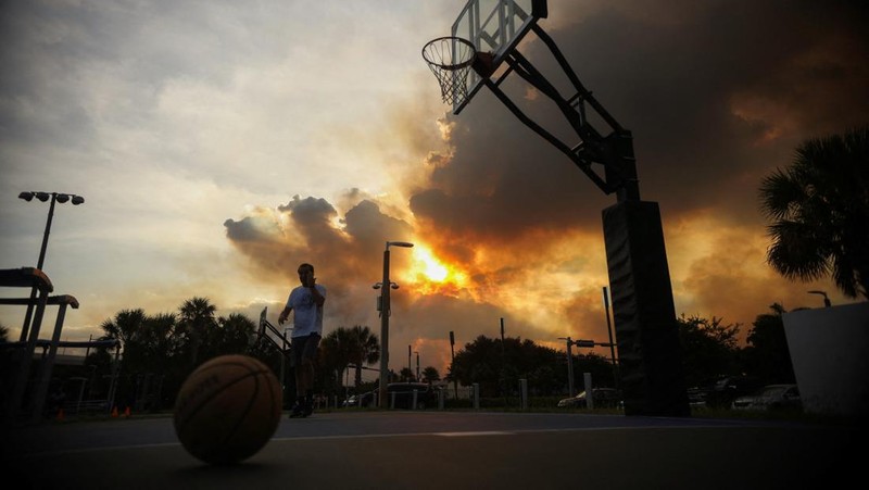 Seorang pria bermain bola basket di Doral Legacy Park saat kebakaran semak berkobar relatif dekat dengan lingkungan perumahan Doral di Miami, Florida, AS, 16 Juni 2026.