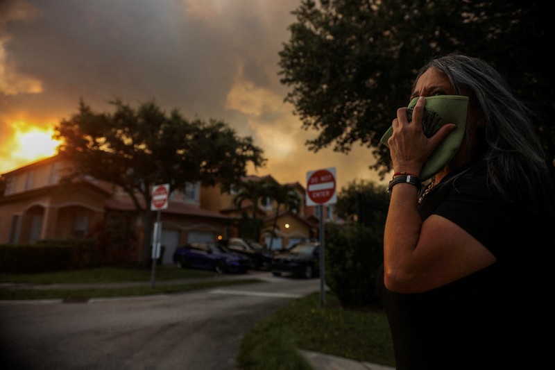 Seorang wanita menutupi wajahnya saat menyaksikan kebakaran semak yang terjadi relatif dekat dengan lingkungan perumahan Doral di Miami, Florida, AS, 16 Juni 2026. (REUTERS/Maria Alejandra Cardona)