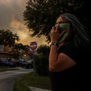 Seorang wanita menutupi wajahnya saat menyaksikan kebakaran semak yang terjadi relatif dekat dengan lingkungan perumahan Doral di Miami, Florida, AS, 16 Juni 2026. (REUTERS/Maria Alejandra Cardona)