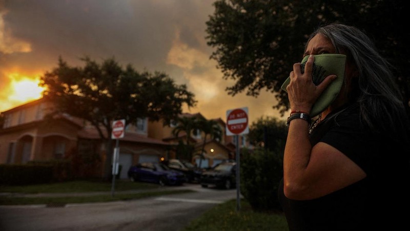 Seorang wanita menutupi wajahnya saat menyaksikan kebakaran semak yang terjadi relatif dekat dengan lingkungan perumahan Doral di Miami, Florida, AS, 16 Juni 2026. (REUTERS/Maria Alejandra Cardona)