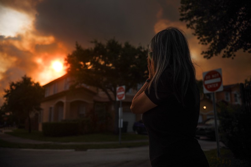 Seorang wanita menutupi wajahnya saat menyaksikan kebakaran semak yang terjadi relatif dekat dengan lingkungan perumahan Doral di Miami, Florida, AS, 16 Juni 2026. (REUTERS/Maria Alejandra Cardona)