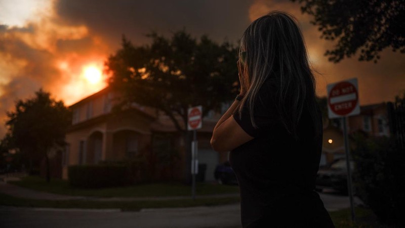 Seorang wanita menutupi wajahnya saat menyaksikan kebakaran semak yang terjadi relatif dekat dengan lingkungan perumahan Doral di Miami, Florida, AS, 16 Juni 2026.