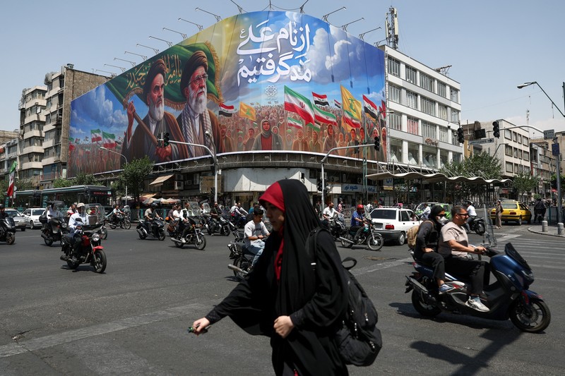 Perempuan Iran berjalan melewati mural anti-AS di sebuah jalan di Teheran, Iran, Senin (15/6/2026). Meski hidup dalam ketidakpastian, sebagian warga Iran berusaha menjalani hari seperti biasa. (via REUTERS/Majid Asgaripour)