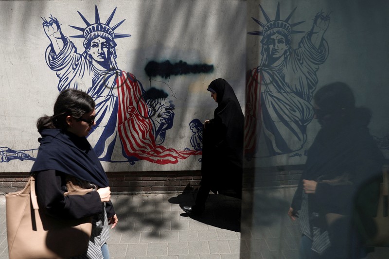 Perempuan Iran berjalan melewati mural anti-AS di sebuah jalan di Teheran, Iran, Senin (15/6/2026). Meski hidup dalam ketidakpastian, sebagian warga Iran berusaha menjalani hari seperti biasa. (via REUTERS/Majid Asgaripour)