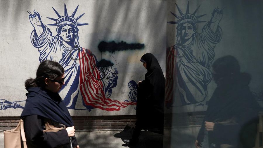 Perempuan Iran berjalan melewati mural anti-AS di sebuah jalan di Teheran, Iran, Senin (15/6/2026). Meski hidup dalam ketidakpastian, sebagian warga Iran berusaha menjalani hari seperti biasa. (via REUTERS/Majid Asgaripour)
