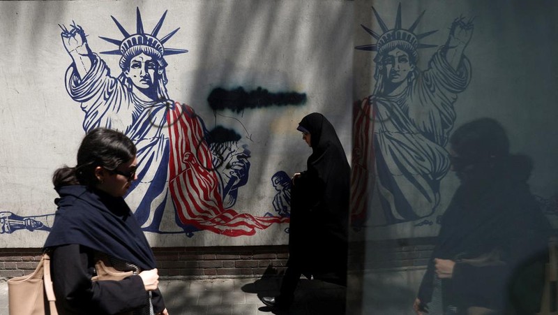 Perempuan Iran berjalan melewati mural anti-AS di sebuah jalan di Teheran, Iran, Senin (15/6/2026). Meski hidup dalam ketidakpastian, sebagian warga Iran berusaha menjalani hari seperti biasa. (via REUTERS/Majid Asgaripour)