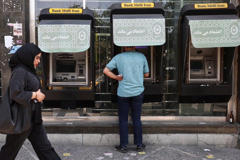 Perempuan Iran berjalan melewati mural anti-AS di sebuah jalan di Teheran, Iran, Senin (15/6/2026). Meski hidup dalam ketidakpastian, sebagian warga Iran berusaha menjalani hari seperti biasa. (via REUTERS/Majid Asgaripour)