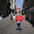 Seorang wanita menggunakan payung merah untuk berteduh dari matahari saat berjalan di jalanan Nantes ketika suhu meningkat selama gelombang panas yang melanda sebagian besar Prancis, 22 Juni 2026. (REUTERS/Stephane Mahe)