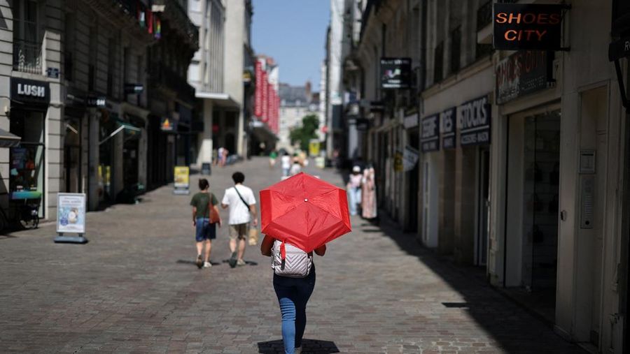 Seorang wanita menggunakan payung merah untuk berteduh dari matahari saat berjalan di jalanan Nantes ketika suhu meningkat selama gelombang panas yang melanda sebagian besar Prancis, 22 Juni 2026.