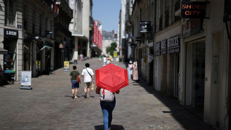 Seorang wanita menggunakan payung merah untuk berteduh dari matahari saat berjalan di jalanan Nantes ketika suhu meningkat selama gelombang panas yang melanda sebagian besar Prancis, 22 Juni 2026.