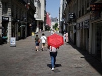 Seorang wanita menggunakan payung merah untuk berteduh dari matahari saat berjalan di jalanan Nantes ketika suhu meningkat selama gelombang panas yang melanda sebagian besar Prancis, 22 Juni 2026. (REUTERS/Stephane Mahe)