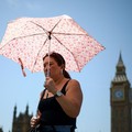 Seorang wanita menggunakan payung untuk melindungi diri dari matahari saat berjalan di dekat Gedung Parlemen, di tengah cuaca panas di London, Inggris, 23 Juni 2026. (REUTERS/Guglielmo Mangiapane)