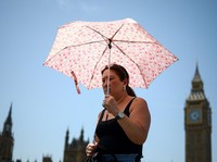 Seorang wanita menggunakan payung untuk melindungi diri dari matahari saat berjalan di dekat Gedung Parlemen, di tengah cuaca panas di London, Inggris, 23 Juni 2026. (REUTERS/Guglielmo Mangiapane)