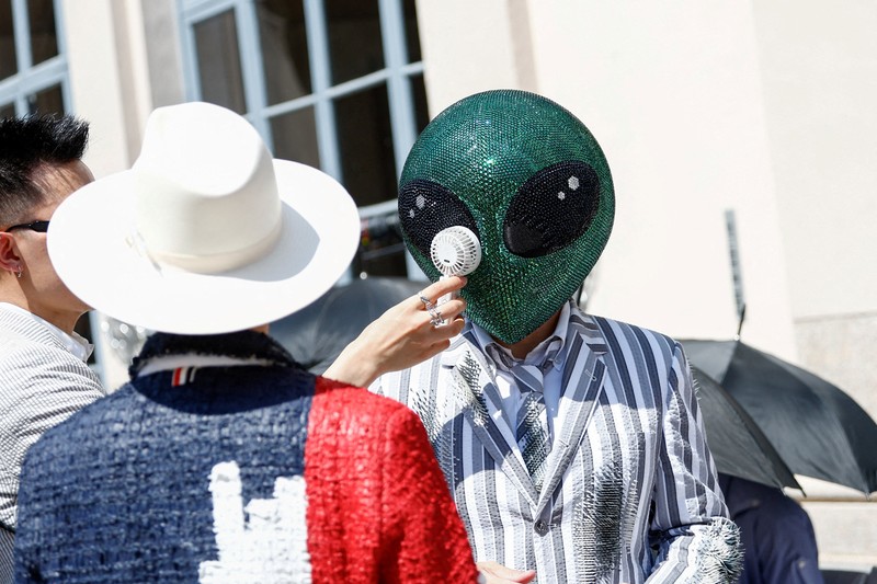 Seseorang yang mengenakan topeng alien duduk di antara penonton dengan kipas angin listrik portabel selama peragaan koleksi busana pria Musim Semi/Musim Panas 2027 karya Thom Browne sebagai bagian dari Milan Fashion Week, di Milan, Italia, 22 Juni 2026. (REUTERS/Alessandro Garofalo)