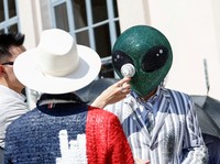Seseorang yang mengenakan topeng alien duduk di antara penonton dengan kipas angin listrik portabel selama peragaan koleksi busana pria Musim Semi/Musim Panas 2027 karya Thom Browne sebagai bagian dari Milan Fashion Week, di Milan, Italia, 22 Juni 20