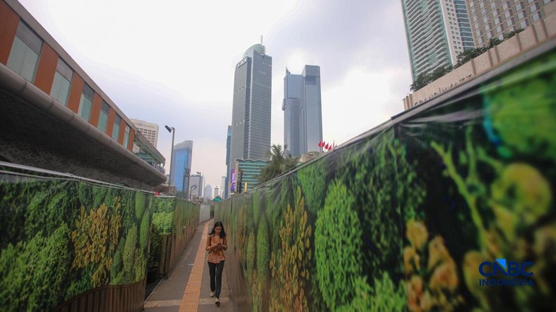 Warga berjalan kaki melewati trotoar darurat yang didekorasi menyerupai lorong taman labirin di atas kawasan proyek pengembangan kawasan Stasiun MRT Bundaran Hotel Indonesia, Jakarta, Rabu (24/6/2026).