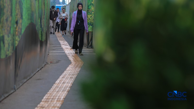 Warga berjalan kaki melewati trotoar darurat yang didekorasi menyerupai lorong taman labirin di atas kawasan proyek pengembangan kawasan Stasiun MRT Bundaran Hotel Indonesia, Jakarta, Rabu (24/6/2026). (CNBC Indonesia/Faisal Rahman)