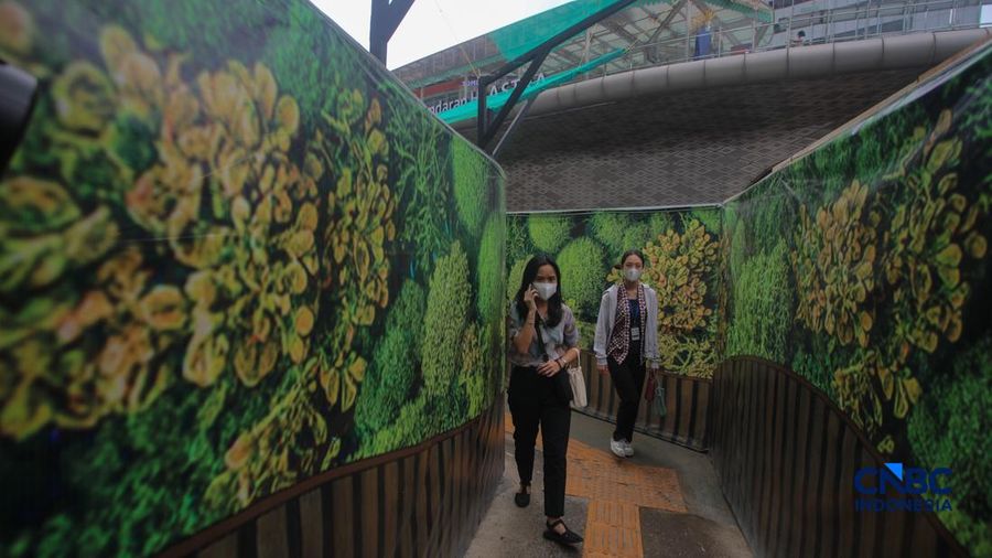Warga berjalan kaki melewati trotoar darurat yang didekorasi menyerupai lorong taman labirin di atas kawasan proyek pengembangan kawasan Stasiun MRT Bundaran Hotel Indonesia, Jakarta, Rabu (24/6/2026).