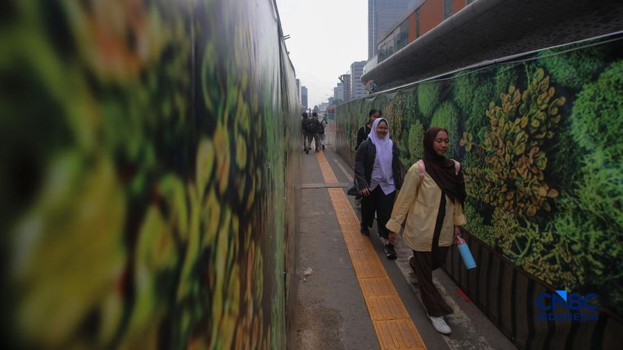 Warga berjalan kaki melewati trotoar darurat yang didekorasi menyerupai lorong taman labirin di atas kawasan proyek pengembangan kawasan Stasiun MRT Bundaran Hotel Indonesia, Jakarta, Rabu (24/6/2026).