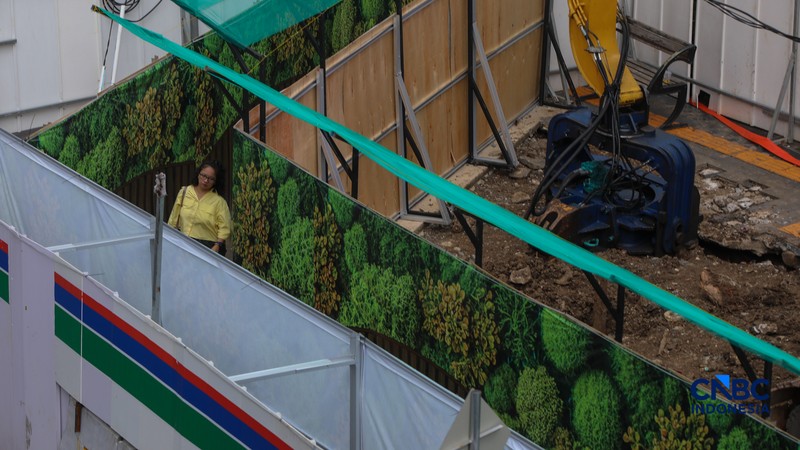 Warga berjalan kaki melewati trotoar darurat yang didekorasi menyerupai lorong taman labirin di atas kawasan proyek pengembangan kawasan Stasiun MRT Bundaran Hotel Indonesia, Jakarta, Rabu (24/6/2026). (CNBC Indonesia/Faisal Rahman)