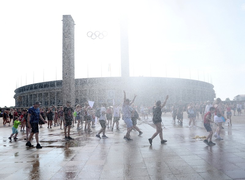 Orang-orang menikmati semprotan air dari meriam air polisi di depan stadion Olimpiade Olympiastadion selama gelombang panas yang sedang berlangsung di Berlin, Jerman, 28 Juni 2026. (REUTERS/Maryam Majd)