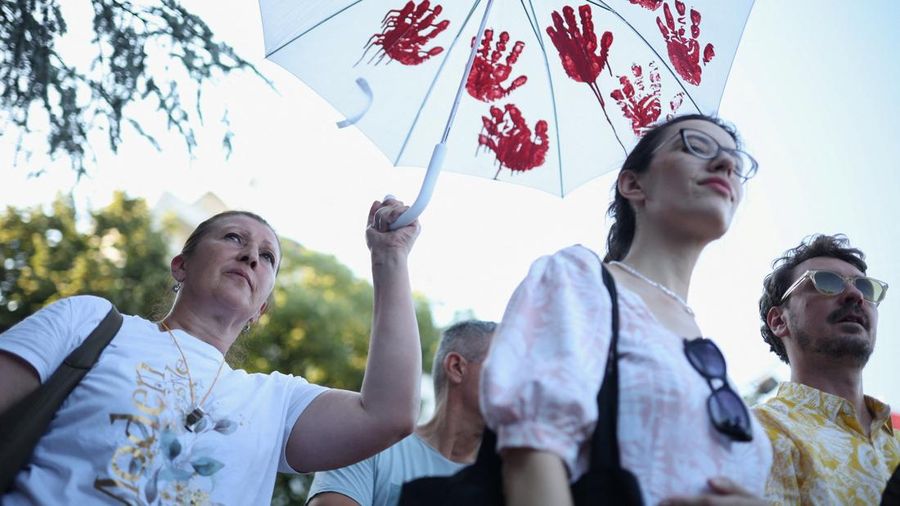 Seorang demonstran memegang payung dengan cetakan tangan cat merah sementara orang-orang berkumpul untuk protes sebagai bagian dari gerakan anti-pemerintah nasional yang dipicu oleh runtuhnya kanopi stasiun kereta api Novi Sad yang menewaskan banyak orang pada November 2024, menyusul pengumuman pengunduran diri Presiden Serbia Aleksandar Vucic, di Kraljevo, Serbia, 28 Juni 2026.