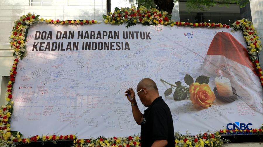 Pengemudi ojek online melintas di depan karangan bunga