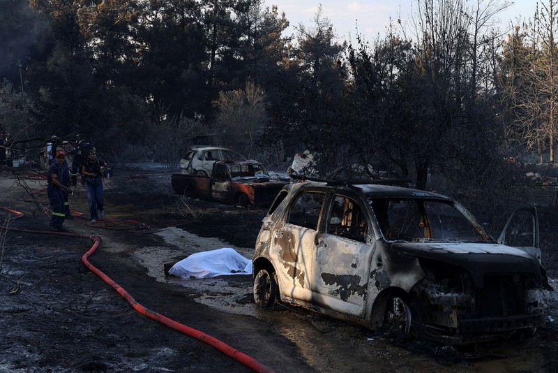 Jenazah korban kebakaran hutan tergeletak tertutup kain di samping mobil yang terbakar setelah kebakaran hutan di dekat desa Liti, Thessaloniki, Yunani, 30 Juni 2026. (REUTERS/Alexandros Avramidis)