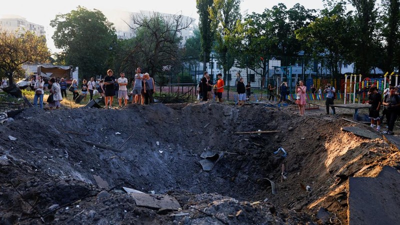 Warga berdiri di samping kawah yang terbentuk di lokasi tersebut akibat serangan rudal dan pesawat tak berawak Rusia semalaman, di tengah serangan Rusia terhadap Ukraina, di Kyiv, Ukraina, 2 Juli 2026.
