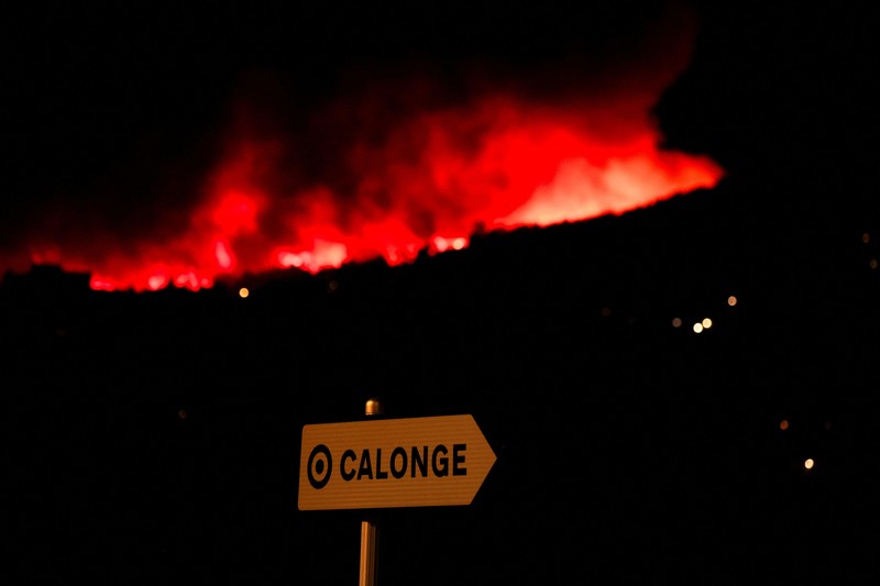 People look on as flames and smoke from a wildfire rise near Calonge, Spain, July 4, 2026. REUTERS/Bruna Casas     TPX IMAGES OF THE DAY