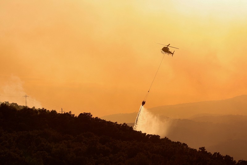 People look on as flames and smoke from a wildfire rise near Calonge, Spain, July 4, 2026. REUTERS/Bruna Casas     TPX IMAGES OF THE DAY