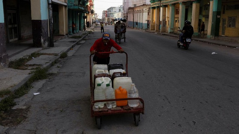 Seorang pria mendorong gerobak dorong berisi wadah air plastik saat Kuba berjuang untuk memulihkan aliran listrik setelah runtuhnya jaringan listrik nasional sehari sebelumnya, menyebabkan jutaan orang masih tanpa listrik di seluruh negara kepulauan Karibia itu, di Havana, Kuba, 7 Juli 2026.