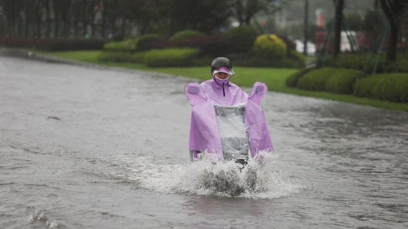 A person rides an electric scooter through a flooded road after heavy rain brought by Typhoon Bavi in Wenzhou, Zhejiang province, China July 12, 2026.