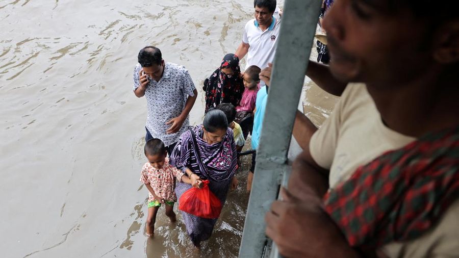 Orang-orang berjalan di sepanjang jalan yang tergenang banjir setelah hujan deras di Dhaka, Bangladesh, 12 Juli 2026.