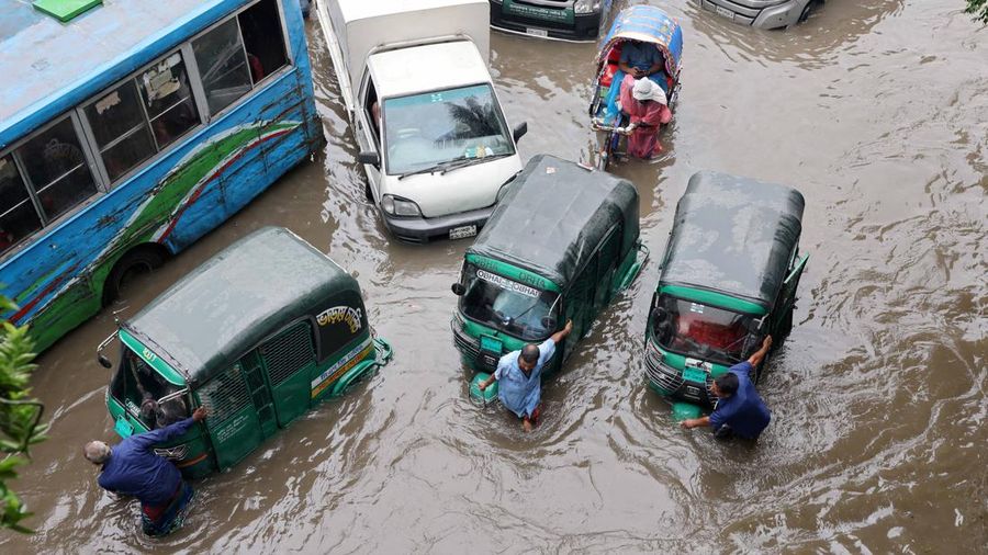 Para pengemudi mendorong becak motor mereka melewati jalan yang tergenang banjir setelah mesin kendaraan mereka mogok akibat hujan deras di Dhaka, Bangladesh, 12 Juli 2026.