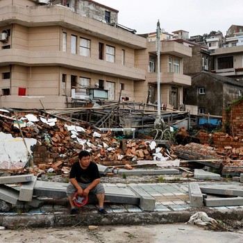Seseorang duduk di samping tembok yang runtuh pasca Topan Bavi di desa pesisir Dongsha, Taizhou, provinsi Zhejiang, China, 12 Juli 2026. (REUTERS/Go Nakamura)