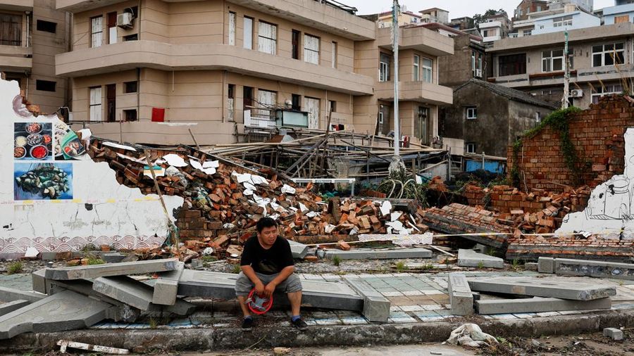 Seseorang duduk di samping tembok yang runtuh pasca Topan Bavi di desa pesisir Dongsha, Taizhou, provinsi Zhejiang, China, 12 Juli 2026. (REUTERS/Go Nakamura)