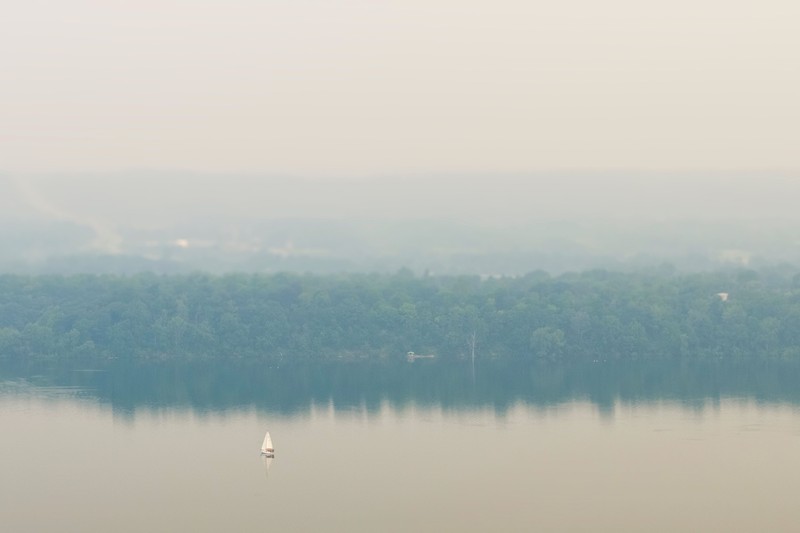 Seseorang menunjuk ke cakrawala saat menaiki feri dari Pulau Toronto, sementara asap kebakaran hutan dari Ontario barat laut memenuhi langit, ditambah dengan gelombang panas yang hebat, memicu peringatan kesehatan dan seruan kepada warga untuk membatasi aktivitas di luar ruangan di Toronto, Ontario, Kanada, 15 Juli 2026. (REUTERS/Carlos Osorio)