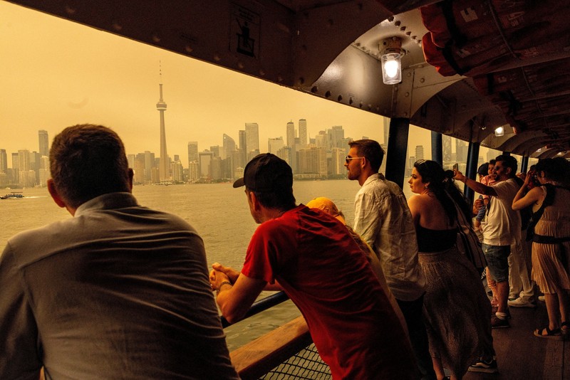 Seseorang menunjuk ke cakrawala saat menaiki feri dari Pulau Toronto, sementara asap kebakaran hutan dari Ontario barat laut memenuhi langit, ditambah dengan gelombang panas yang hebat, memicu peringatan kesehatan dan seruan kepada warga untuk membatasi aktivitas di luar ruangan di Toronto, Ontario, Kanada, 15 Juli 2026. (REUTERS/Carlos Osorio)