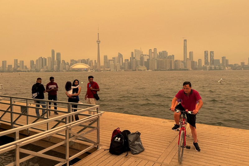 Seseorang menunjuk ke cakrawala saat menaiki feri dari Pulau Toronto, sementara asap kebakaran hutan dari Ontario barat laut memenuhi langit, ditambah dengan gelombang panas yang hebat, memicu peringatan kesehatan dan seruan kepada warga untuk membatasi aktivitas di luar ruangan di Toronto, Ontario, Kanada, 15 Juli 2026. (REUTERS/Carlos Osorio)