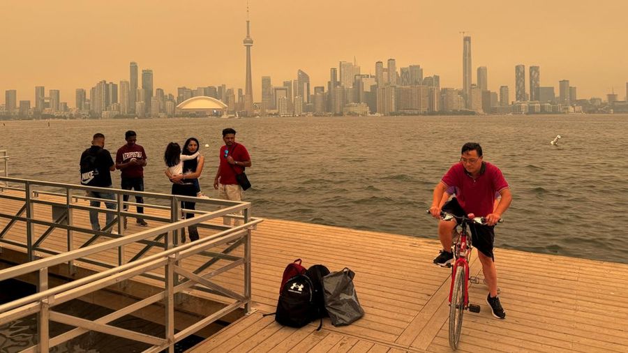 Para pengunjung berdiri sambil memandang cakrawala pusat kota yang tertutup asap kebakaran hutan selama gelombang panas, seperti yang terlihat dari Kepulauan Toronto di Danau Ontario, di Toronto, Ontario, Kanada, 15 Juli 2026.